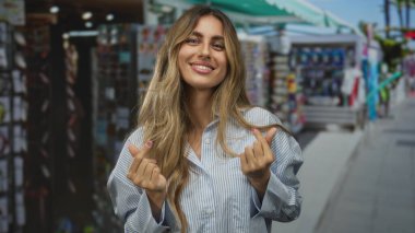 Sarışın kadın gülümsüyor ve hareketli market tezgahında kalp hareketi yapıyor; sevgi dolu neşe flörtü.