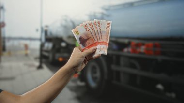 Kentsel geçmişe sahip şehir sokaklarında Norveç kronu banknotları tutan adam, halka açık bir ortamda finansal temalar sergiliyor..