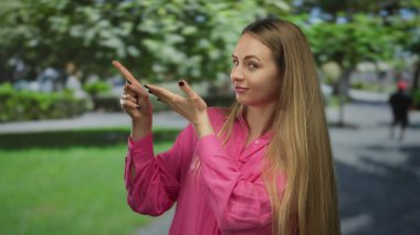 Rahat bir ifadeyle canlı yeşil bir parkta güneşli bir günün sakin, açık hava ortamını gösterirken iyi bir işaret veren bir kadın..