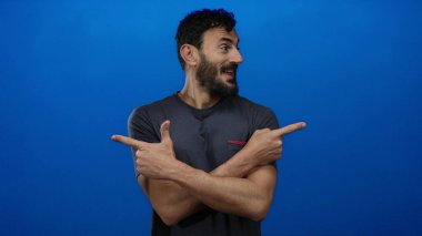 Günlük gömlekli İspanyol bir adam gülümsüyor ve parlak mavi bir arkaplanı işaret ediyor. Olumlu duygular ve gelişigüzel davranışlar sergiliyor..