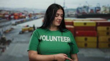 Renkli konteynırlar ve teknelerle deniz kenarındaki limanı işaret eden gönüllü genç kadın açık havada gönüllü ruhun altını çiziyor..