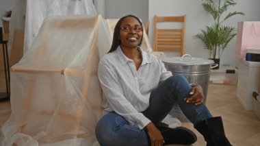 Yeni bir evde kutlayan bir kadın. Paketleri açılmış bir şekilde yerde oturuyor. Oturma odasında heyecanını ve neşesini dile getiriyor..