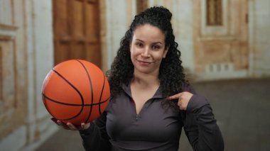 Eski bir üniversite avlusunda İspanyol bir kadın elinde basketbol topuyla kendini göstererek atletik ruhu ve akademik arkaplanı canlandırıyor..