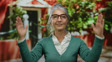 Canlı bir sokak arkaplanında el hareketleriyle gri saçlı yaşlı bir kadın şehir ortamında kendine güven ve dışavurumculuk gösteriyor..