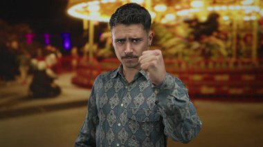 Fonda bulanık ışıklar olan canlı bir panayırda kararlı bir ifadeye sahip genç adam, gündelik ama yoğun bir odak ve enerji anı yakalıyor..