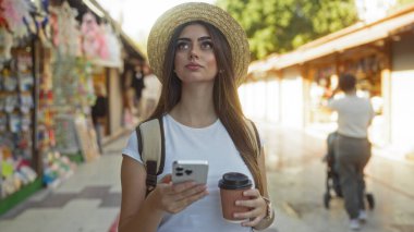 Kadın elinde kahve ve telefon ile şehir pazarını keşfediyor, şık bir şapka takıyor, güneş ışığı caddeye hafifçe vuruyor, hayat dolu şehir hayatının özünü yakalıyor..