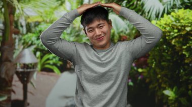 Genç adam yemyeşil bir parkta gülümsüyor. Neşeli bir yüz ifadesi sergiliyor. Sakin bir açık hava ortamında..