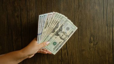 Ahşap arka planda Amerikan doları tutan kadın elinde birden fazla banknot tutuyor..