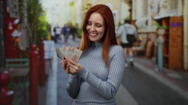 Canlı bir şehir caddesinde elinde İsveç banknotları tutan, neşeli bir ifade sergileyen ve açık bir şehir ortamında para birimini ön plana çıkaran bir kadın..