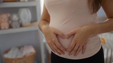 Bebek odasında elleri karnında, beşikte, anne sevgisini ve beklentisini simgeleyen bir kalp oluşturan hamile kadın..