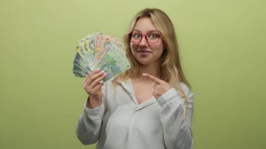 Elinde Romen lei banknotları tutan kadın yeşil duvarı işaret ederek para birimi zenginliğini güvenle gösteren bir gülümseme sergiliyor.