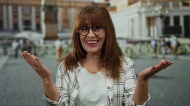 İspanyol kıdemli kadın, Aziz Peter Meydanı, Vatikan 'da el kol hareketi yaparken sevinçle gülümsüyor, tarihi mimariyle canlı bir açık hava atmosferi yakalıyor..