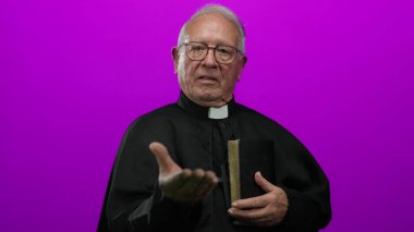 Başrahip elinde bir kitapla pembe bir arka plana karşı el kol hareketi yaparak inanç ve maneviyatı aktarıyor..