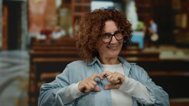 Kilisenin içinde gülümseyen bir kadın elleriyle kalp hareketi yapıyor, İspanyol kültüründe sıcak bir etkileşim yakalıyor..