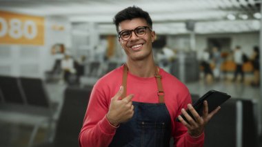 Yoğun havaalanı terminalinde önlüklü genç bir adam. İçerde güvenle gülümseyerek çekici bir şekilde poz veriyor..