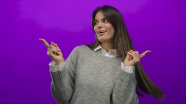 Süveter giyen İspanyol kadın her iki tarafı da işaret ediyor canlı mor duvarlara karşı neşeli pozlarla izole edilmiş..