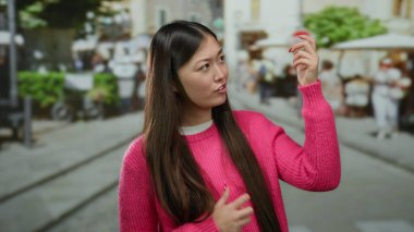 Şehir sokaklarında canlı şehir arkaplanı olan canlı pembe süveterle gitar çalan kadın taklidi yapıyor..