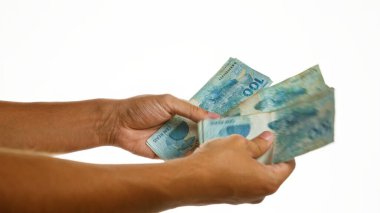 Beyaz bir arkaplan üzerinde Brezilya 'nın gerçek banknotlarını tutan eller, döviz kurunu veya mali işlemleri gösteriyor