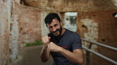 Roma 'daki eski bir kasabada sakallı, İspanyol bir adam. Arka planda bulanık tuğla duvarlarla güvenle duruyor. Dinamik bir duruş yakalıyor..