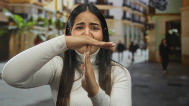 Bulanık yayalar ve binalarla çevrili bir şehir sokağında duran genç İspanyol kadın, aciliyet ve modern şehir yaşamını aktarıyor..