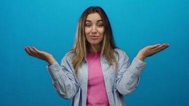 Mavi arka plan önünde ellerini kaldırmış, komik bir jest yapan bir kadın. Günlük giysiler giymiş, neşeli bir ifadeyi yansıtıyor..