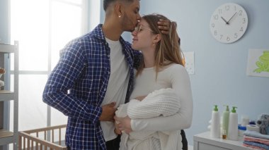 Bir çift, sıcak yatak odasında bebeği kucaklarken sevgi dolu bir şekilde kucaklaşır. Yumuşak doğal ışık eşliğinde huzurlu bir evde aile sevgisini ve beraberliği sembolize eder..