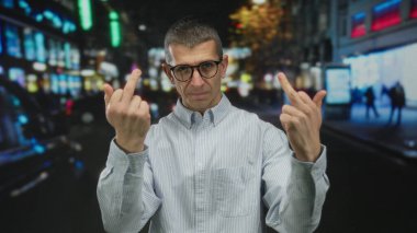 Gözlüklü bir adam gece aydınlanmış şehir caddesinde kırıcı hareketlerde bulunuyor. Açık bir şehir ortamında meydan okuma ve tavır sergiliyor..