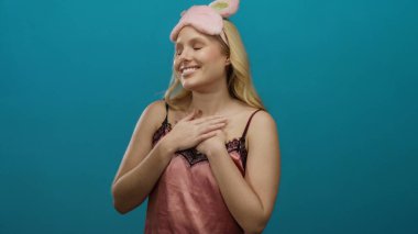 Mavi arka planda duran pembe gecelikli kadın, elleri göğsünde bir içerik ifadesi gösteriyor..