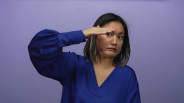 İzole edilmiş mor bir duvarın önünde mavi bir bluz giymiş el hareketleriyle yüz ifadelerini sergileyen bir kadın.