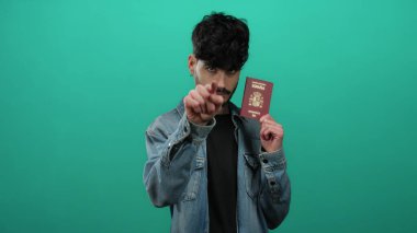 Yeşil duvara karşı İspanyol pasaportu taşıyan bir adam seyahat amacıyla kot ceketli ve ciddi ifadeli kimlik teşhisi koyuyor..