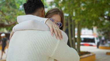 Açık bir şehir parkında ağaçlarla ve bulanık bir şehir zeminiyle sevgi dolu kucaklaşan bir çift, kamusal alanda kadın ve erkek arasındaki samimiyet ve bağlantıyı aktarıyor..