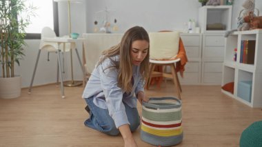 Bebek odasındaki oyuncakları renkli sepetle temizleyen kadın bebek mobilyası ve dekorla çevrili..