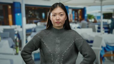 Kapalı gözlü bir kadın, şehir restoranının terasında dikiliyor. Açık havada gri bir kazak giyiyor ve yüzünde odaklanmış bir ifade var..