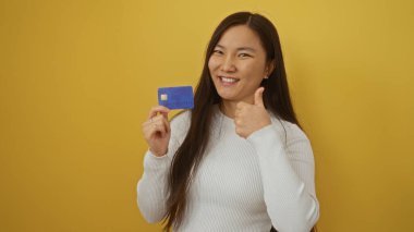 Elinde kredi kartıyla gülümseyen bir kadın sarı arka plana başparmak işareti veriyor. Bu da başarıyı ve parlak bir ortamda finansal güveni simgeliyor..