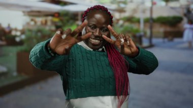 Kırmızı örgülü gülümseyen kadın bir restoranın dışındaki terasta zafer jesti yapıyor..