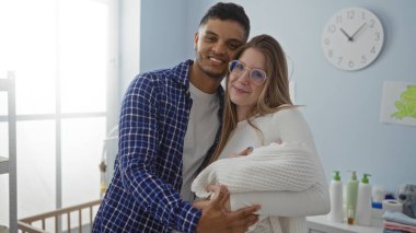 Yatak odasındaki çift yeni doğmuş bebeği bir arada tutuyor, aile bağlarını ve sevgiyi modern dekorasyonla sergiliyor..