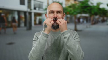 Sakallı bir adam şehir caddesinde gri bir kazak giyip, şehir ortamını beğendiğini ya da beğendiğini ifade ediyor..