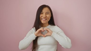 Pembe arka planda gülümseyen bir kadın, genç Asyalı bir kadın kalp şekli oluşturuyor, izole edilmiş bir portrede elleri ile, mutluluk ve pozitifliği ifade ediyor..