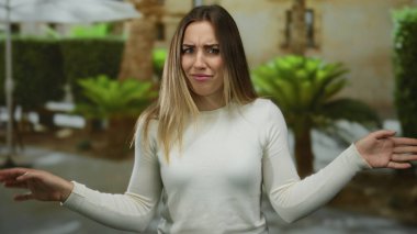 Sokakta elini kaldırmış yeşil bitkilerin arasında şaşkınlığını ifade eden bir kadın..