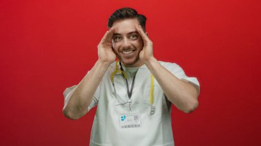 Steteskopla gülümseyen genç bir doktor, parlak kırmızı bir arkaplanda izole edilmiş, neşeli ve profesyonel bir tavır sergiliyor..