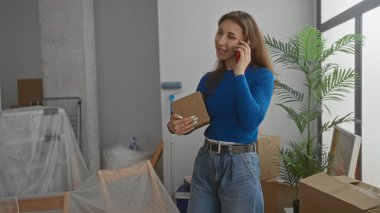 Yeni dairede kutular ve saksılarla çevrili bir kadın telefonla konuşuyor. Evin içini gösteriyor. Oturma odasında taşınıyor..