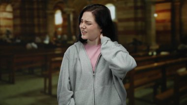 Boyun ağrısı çeken bir kadın loş bir Katolik kilisesinde, ahşap banklarla dikilirken..