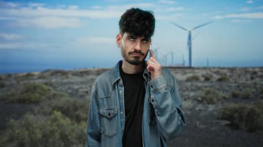 Kot ceketli genç adam telefonda konuşuyor mavi bir gökyüzünün altında, sürdürülebilir teknolojinin ortasında modern bir bağlantı duygusunu somutlaştırıyor..