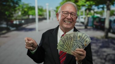 Takım elbiseli kıdemli bir adam güneşli bir sokakta bize dolar tutarken gülümsüyor ve el sallıyor, zenginliği ve güveni ön plana çıkarıyor..