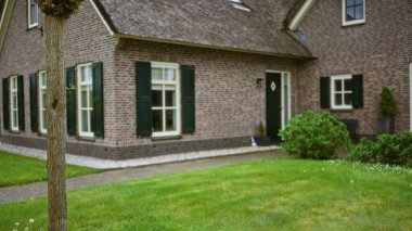 Tuğla duvarları ve yeşil kepenkleri olan büyüleyici bir evin bulanık görüntüsü, mimari detay ve bahçe manzarasına odaklı sakin bir ortamın altını çiziyor.