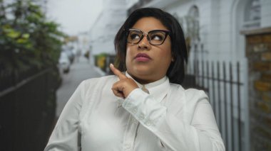 Beyaz gömlekli kadın şehir sokaklarında farklı duygular ve jestler gösteriyor, şehir Latin Amerika ortamında çeşitlilik ve vücut pozitifliğini vurguluyor..