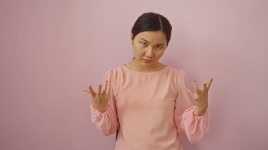 Duygularını pembe arka planda ifade eden kadın, pembe bluz giyiyor; genç, çekici, Asyalı, izole olmuş yetişkin boş bir duvar üzerinde duygu sergiliyor.