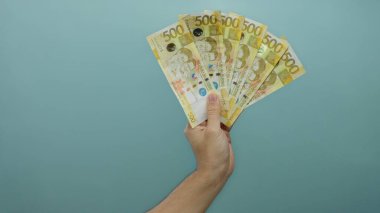 Adamın elinde mavi arka planda Filipinli peso banknotları var. İzole edilmiş bir ortamda para ve finansal temalar sergiliyor..