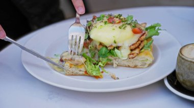 Ellerin gurme yumurtalarını kesiyor. Sıcak bir kafede beyaz bir tabakta taze yeşilliklerle birlikte..