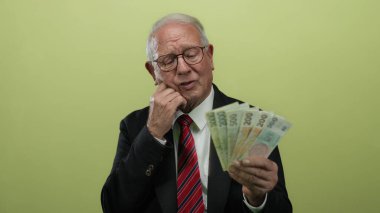 Takım elbiseli kıdemli bir adam, Koruna 'nın paralarını izole edilmiş sarı bir arka plan üzerinde incelikle tutuyor..